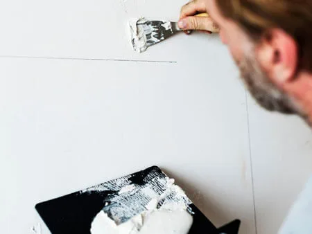 man applying spackle with a putty knife on wall