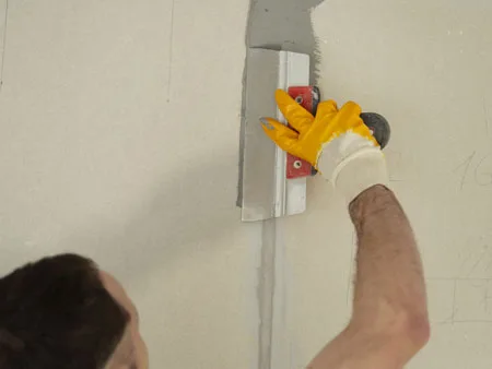 contractor using a wide knife to apply joint compound