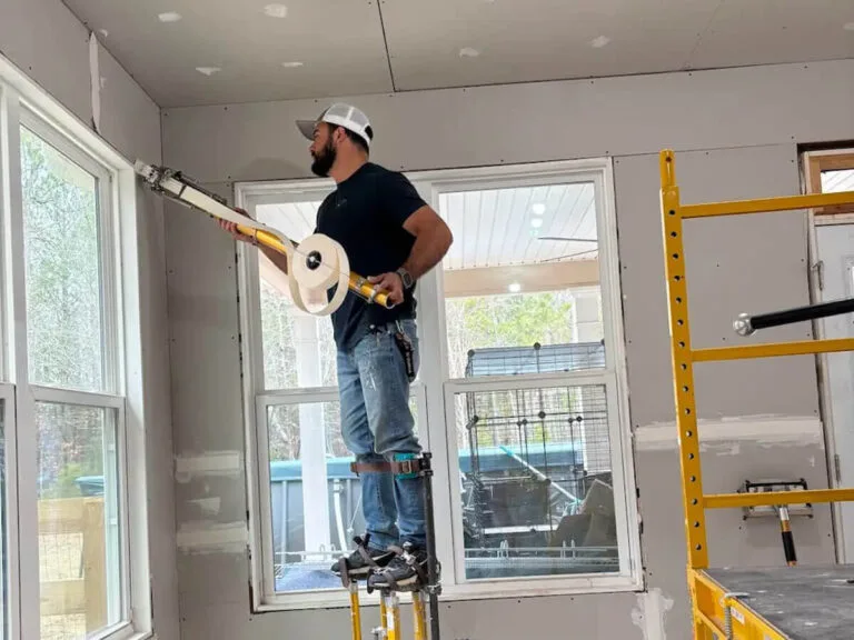 drywall taper on stilts using an automatic taping tool to finish seams in a new room